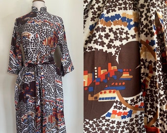 May include: A midi-length dress with a mandarin collar and three-quarter sleeves, featuring a white base with a brown floral pattern and geometric shapes in red, blue, and tan. The dress includes a matching fabric tie belt at the waist.