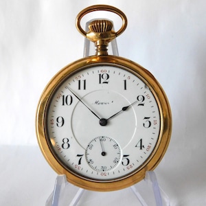 Könnte beinhalten: Eine goldfarbene Taschenuhr mit weißem Zifferblatt, schwarzen Zeigern und schwarzen Ziffern. Die Uhr hat ein kleines Sekunden-Zifferblatt und eine goldene Aufzugswelle. Auf dem Zifferblatt steht "Howw".