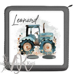 Könnte beinhalten: Ein graues und weißes personalisiertes quadratisches Kissen mit dem Namen "Leonard" darauf gedruckt. Das Kissen zeigt eine Aquarell-Illustration eines blauen Traktors mit braunen Rädern auf einem Feld mit Blumen.