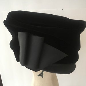 May include: A black velvet hat with a large bow on the side. The hat is sitting on a mannequin's head.