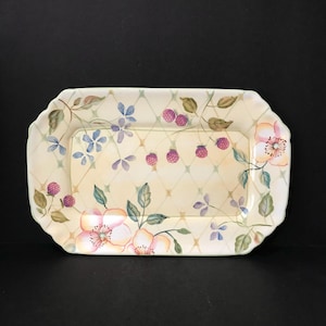 May include: A rectangular ceramic serving platter with scalloped edges, featuring a cream-colored background with a soft green lattice pattern, decorated with hand-painted pink flowers, green leaves, and clusters of small purple raspberries.