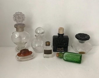 May include: A collection of vintage perfume bottles in various shapes and sizes. The bottles are made of clear and colored glass, with decorative stoppers. One bottle is black with the text "habanita MOLINARD".