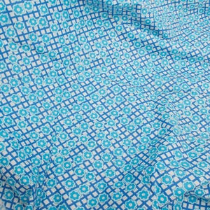 Könnte beinhalten: Ein Stoffstück mit einem sich wiederholenden Muster aus kleinen, hellblauen fünfblättrigen Blüten, die in einem Gitter aus dunkelblauen Linien auf weißem Grund zentriert sind. Das Textil ist drapiert und zeigt Falten auf der Oberfläche.