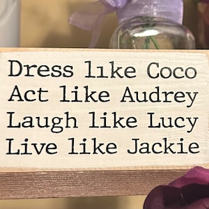 May include: Wooden sign with the text "Dress like Coco, Act like Audrey, Laugh like Lucy, Live like Jackie".