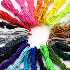 Könnte beinhalten: Eine Sammlung farbenfroher elastischer Kordeln in verschiedenen Farbtönen, darunter Rot, Pink, Orange, Gelb, Grün, Weiß, Braun, Grau, Schwarz, Lila und Blau. Die Kordeln sind gebündelt und geknotet und zeigen eine Reihe lebendiger Farbtöne.