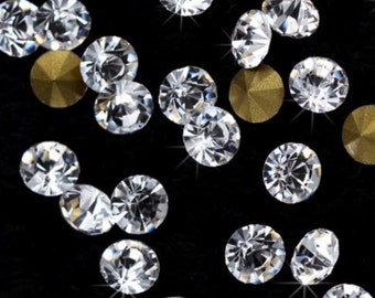 Puede incluir: Primer plano de brillantes pedrería transparente y tachuelas de metal dorado dispersas sobre una superficie negra. Las pedrerías son redondas con múltiples facetas, que reflejan la luz. Las tachuelas doradas también son redondas y tienen un acabado mate. Ideal para nail art o proyectos de manualidades.