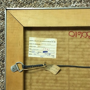 May include: A close-up of a brown wooden frame with a white label attached. The label contains information about a Vasarely serigraph, including the title, artist, year, and price. The label also includes the name of the consignor, Denise Rene, and the rental gallery, Baltimore Museum of Art.