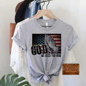 May include: A grey t-shirt with a distressed American flag design and the text "GOD, WE NEED YOU NOW".