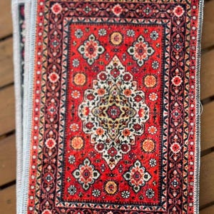 May include: A red, black, and white patterned rug with a fringe border. The rug has a smaller, intricate pattern in the center.