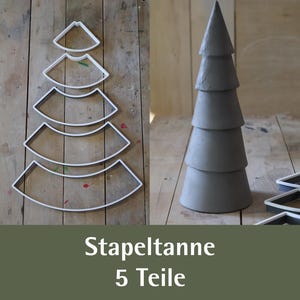 Könnte beinhalten: Ein Set aus fünf weißen, gebogenen, bogenförmigen Stapelteilen, die eine Baum-Silhouette bilden, neben einer fertig montierten grauen, konischen, fünfstufigen Baumstruktur. Der Text "Stapeltanne 5 Teile" ist darunter abgebildet.