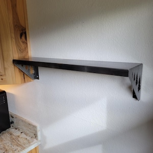 Puede incluir: Una estantería de metal negro con un diseño de árbol en los soportes. La estantería está montada en una pared blanca.