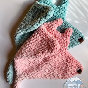May include: Two crocheted hats, one in pink and one in blue, with a long tail. The hats are made with a fluffy yarn and have a textured surface.