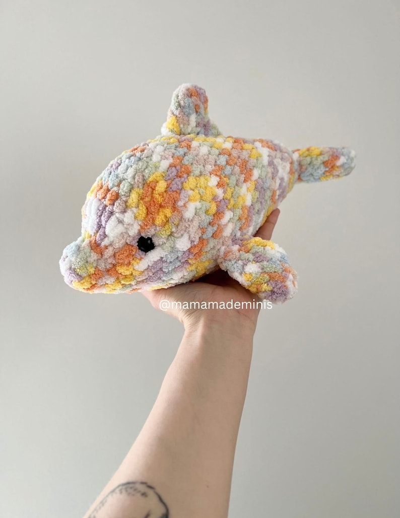 May include: A crocheted dolphin plush toy in a rainbow color pattern. The dolphin is made with a soft, fluffy yarn and has a sweet, friendly expression.