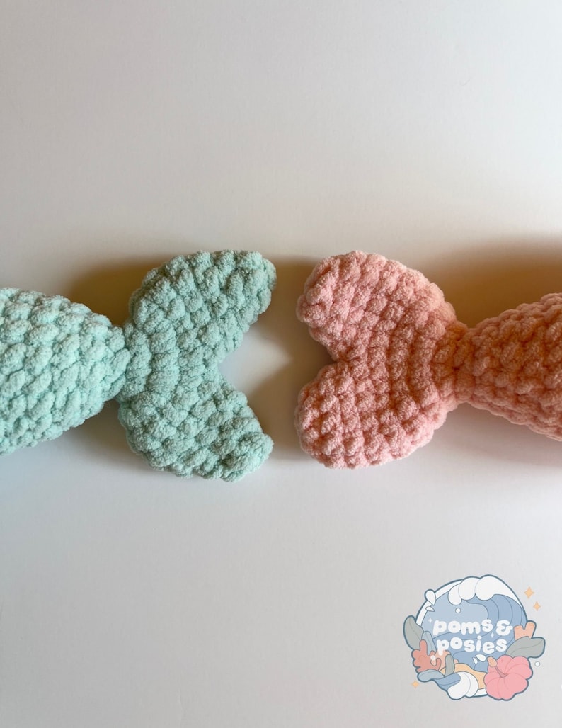 May include: Two crocheted mermaid tails, one in light blue and one in pink, on a white background. The tails are made with a fluffy yarn and have a textured look.