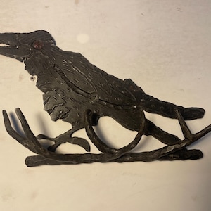 May include: A dark metal wall hook in the shape of a raven on a branch. The raven has an open beak and detailed feather texture. The branch has three curved hooks for hanging items.