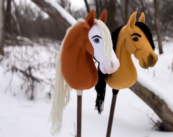 May include: Two brown and tan plush toy horses with long white and black manes. The horses are on wooden sticks and are standing in the snow.