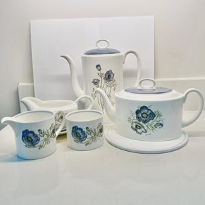 May include: A white tea set with a blue floral pattern. The set includes a teapot, creamer, sugar bowl, and two cups.