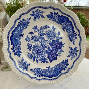 May include: A white ceramic plate with a blue floral design. The plate features a scalloped edge with a heart-shaped border. The center of the plate showcases a detailed blue floral pattern, creating a classic and elegant aesthetic.