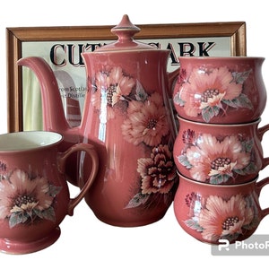 May include: A pink floral tea set with a teapot, creamer, and sugar bowl. The set features a delicate floral pattern with pink, white, and green accents.