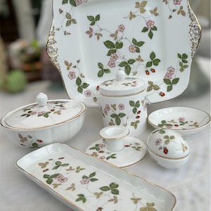 以下が含まれることがあります： イチゴの繊細な模様が施された白い磁器製の食器のセット。セットには、正方形のサービングプレート、蓋付きの丸い皿、小さな丸い皿、長方形の皿、蓋付きの小さな丸い皿、キャンドルホルダーが含まれています。