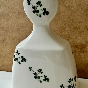 May include: White ceramic bottle stopper with a shamrock design. The stopper has a round top and a rectangular base.