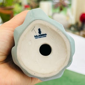 May include: The bottom of a light blue porcelain figurine with the Lladro logo and the words "Hand Made in Spain".
