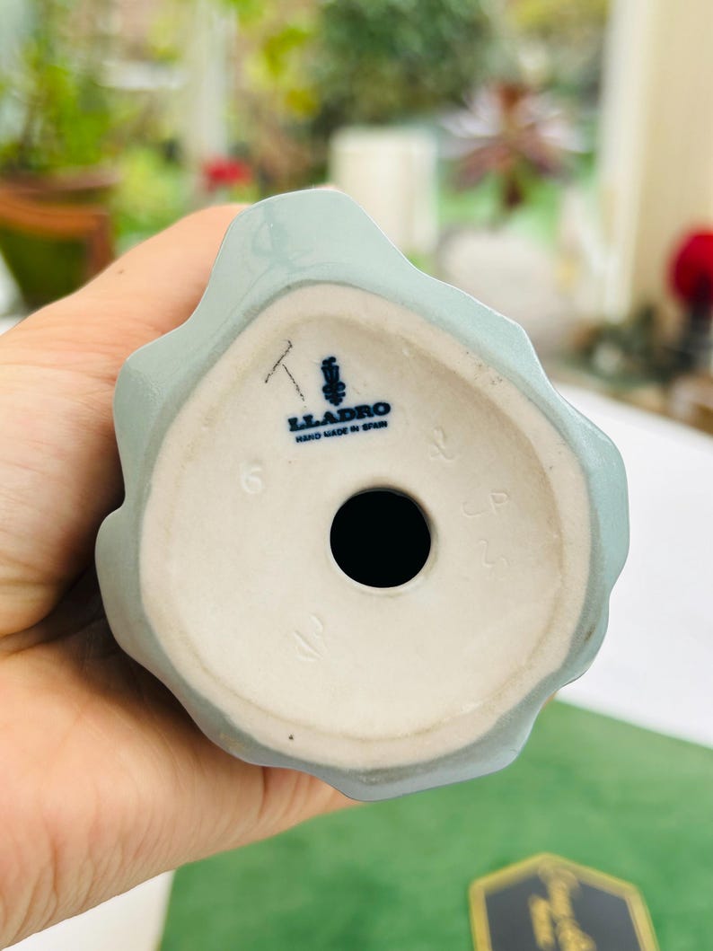 May include: The bottom of a light blue porcelain figurine with the Lladro logo and the words "Hand Made in Spain".