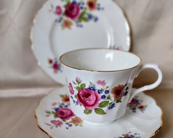 May include: A white teacup and saucer set with a floral pattern. The cup and saucer have a gold trim and feature pink, yellow, and blue flowers.