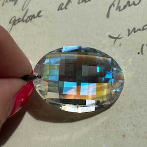May include: A clear crystal prism with a faceted design. The prism is oval shaped and has a rainbow effect.