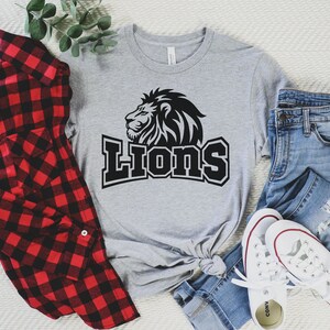 Pode incluir: Uma camiseta cinza com um gr&aacute;fico de le&atilde;o preto e a palavra "Lions" em texto preto.