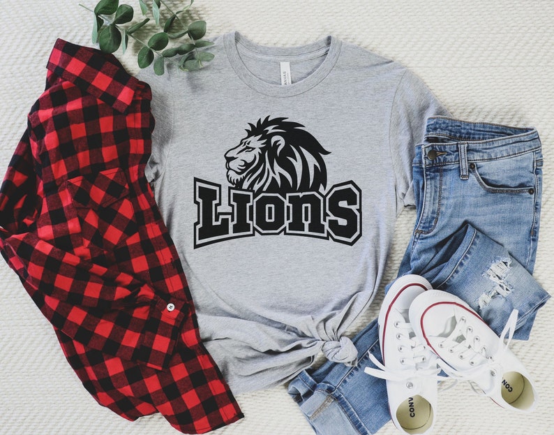 Pode incluir: Uma camiseta cinza com um gr&aacute;fico de le&atilde;o preto e a palavra "Lions" em texto preto.