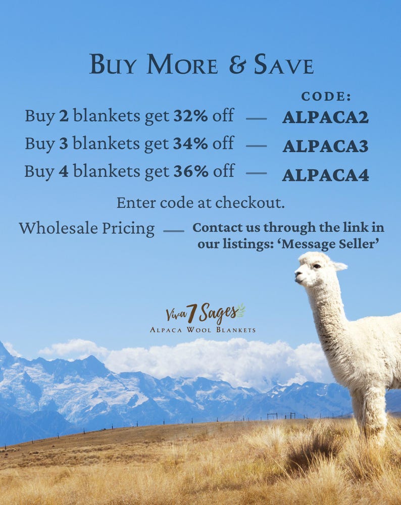 a white llama standing in a field with mountains in the background