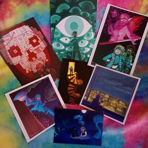 May include: A set of 8 art prints featuring various illustrations. The prints are on white cardstock and have a matte finish. The illustrations include a person with a blue cape, a person with a sword, a person with a blue eye, a person with a staircase, a person with a city view, a person with a moon, and a person with a red and white design.