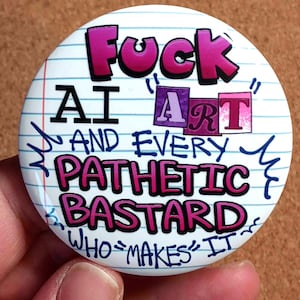 Puede incluir: Un botón redondo blanco con el texto "Fuck AI Art and Every Pathetic Bastard Who Makes It" en letras rosas, moradas y negras. El fondo tiene un diseño de papel rayado.