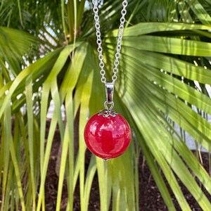 May include: A silver chain necklace with a large, round, red pendant. The pendant has a silver filigree design around the edge.