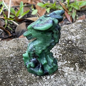 May include: A green and black dragon figurine carved from stone. The dragon is curled up in a defensive position with its wings spread out.