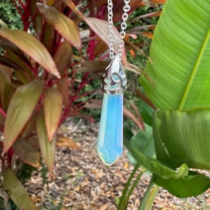 May include: A silver chain necklace with a light blue iridescent crystal pendant. The pendant is shaped like a teardrop and has a silver filigree design around the top.
