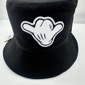 May include: Black bucket hat with a white hand gesture patch on the front.