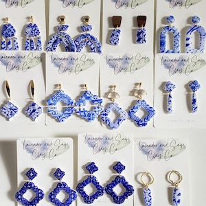 May include: A set of 10 pairs of blue and white ceramic earrings with gold accents. The earrings are displayed on white cards with the text "Lavender and Sage Clay Co."