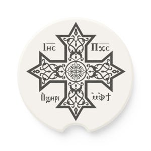 May include: White car coaster with a black, ornate cross design. The cross is centered and features intricate patterns and text. The coaster has a curved cutout for easy removal from a car's cup holder.