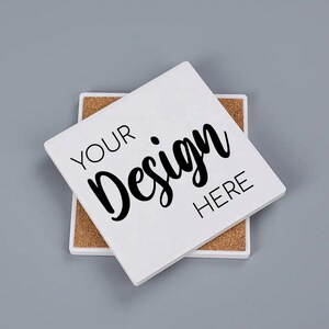 Puede incluir: Posavasos cuadrado de cerámica blanca con el texto "YOUR Design HERE" en escritura negra. El posavasos está sobre una base de corcho, con un segundo posavasos debajo. El fondo es gris liso.