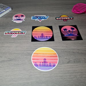 Pu&ograve; includere: Un set di otto adesivi in stile retr&ograve; con un tramonto, palme e il testo "Sunset 86" e "Stay". Gli adesivi sono stampati su carta bianca con una finitura lucida.