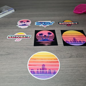 Pu&ograve; includere: Un set di sei adesivi in stile retr&ograve; con un tramonto con palme, una citt&agrave; e il testo "SUNSET 86" e "STAY", il tutto su uno sfondo a effetto legno.