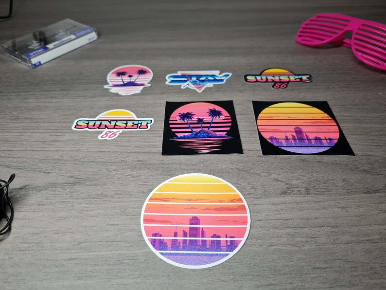 Pu&ograve; includere: Un set di sei adesivi in stile retr&ograve; con un tramonto con palme, una citt&agrave; e il testo "SUNSET 86" e "STAY", il tutto su uno sfondo a effetto legno.