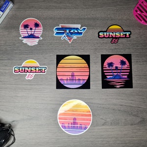 Pu&ograve; includere: Un set di sei adesivi in stile retr&ograve; con scene di tramonto con palme, paesaggi urbani e il testo "Sunset 86" e "Stay Rad".