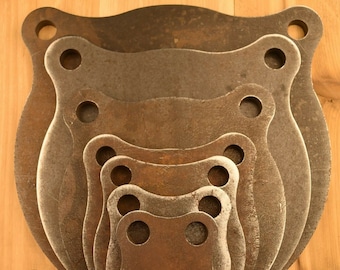 May include: A set of five steel shooting targets, each with a unique shape and size. The targets are nested inside each other, creating a layered effect. The targets are made of dark brown metal with a slightly rusted finish.