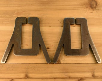May include: Two metal, rusty-brown,  A-frame shaped stands with a square opening in the center. The stands are on a light brown wooden surface.