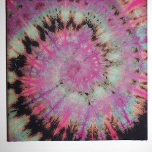 May include: A square canvas with a tie-dye design. The artwork features a spiral pattern with a central focus of pink, surrounded by shades of black, teal, and brown. The canvas is stretched over a wooden frame, ready for display.