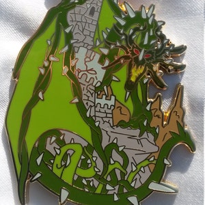 Peut inclure: Une épingle en émail verte et dorée représentant un dragon vert enroulé autour d'une tour de pierre. Le dragon a des dents et des griffes acérées, et ses yeux sont rouges. La tour a un toit pointu et est décorée de détails blancs.