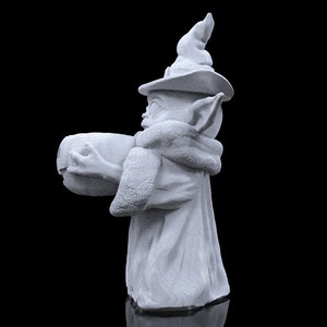 K&ouml;nnte beinhalten: Eine wei&szlig;e Keramikfigur eines Charakters, der einen spitzen Hut und eine lange Robe tr&auml;gt und ein rundes Objekt in der Hand h&auml;lt.